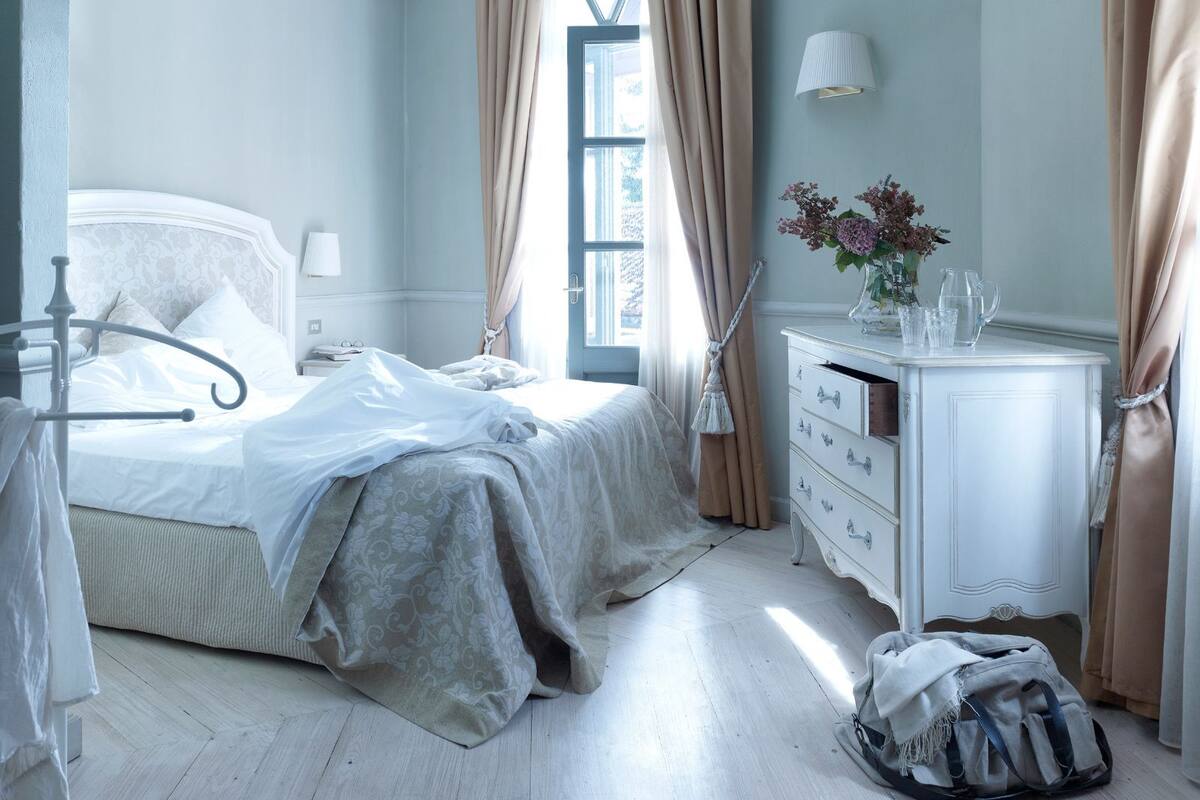 Une chambre à coucher comprenant un lit, une table de chevet, une lampe, une commode et une fenêtre avec des rideaux.