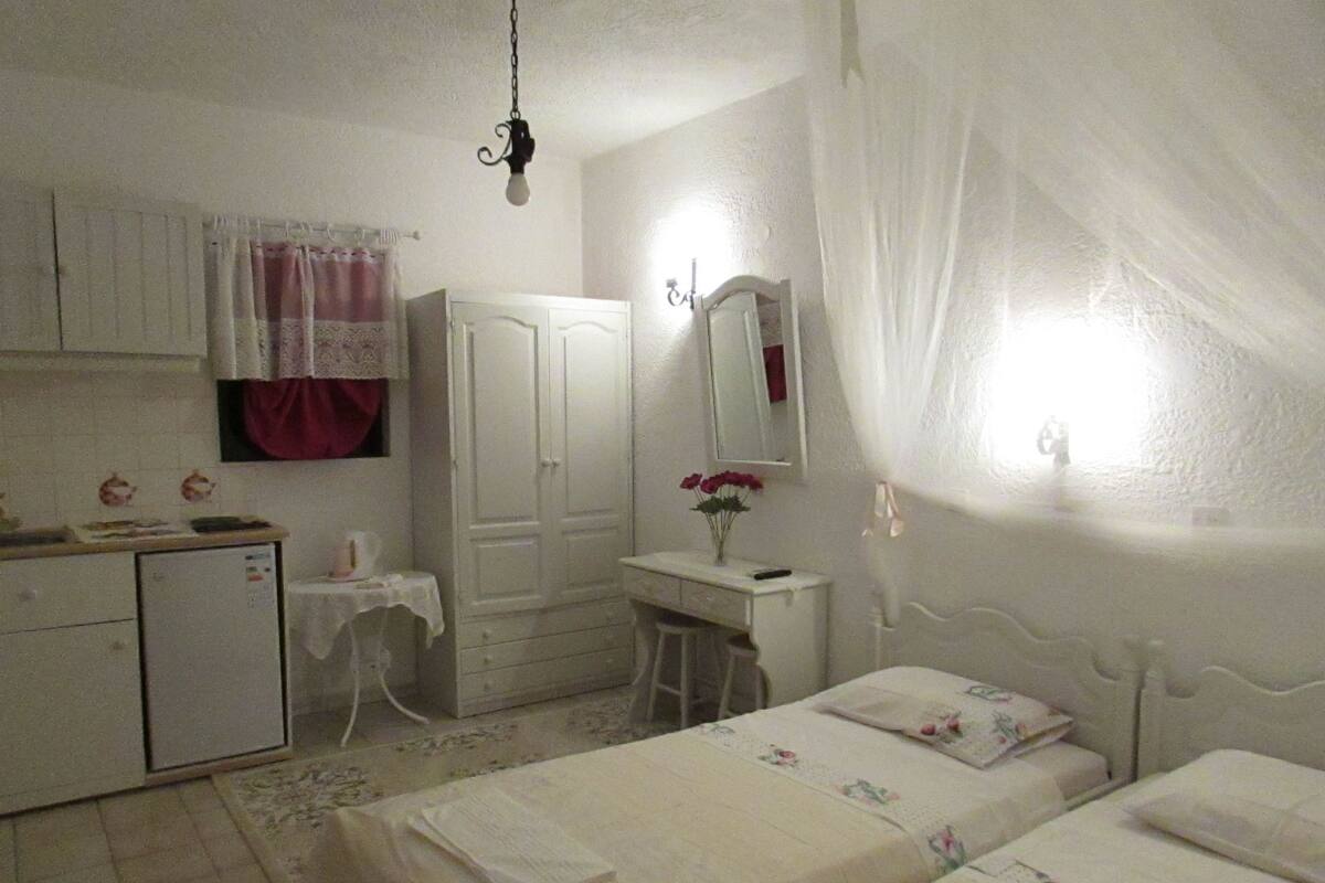 A bedroom with two beds, a desk, a wardrobe, and a small kitchenette.
