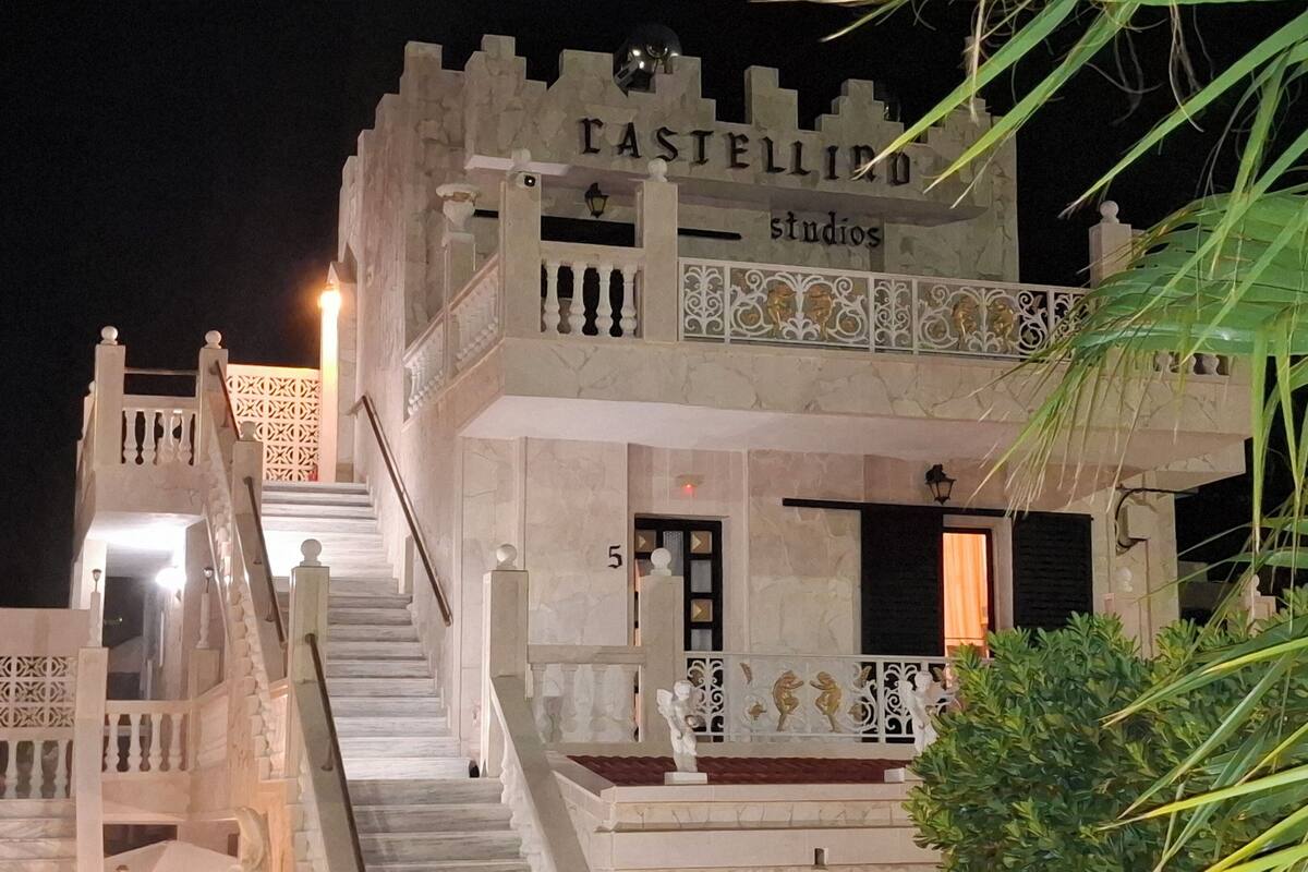 A building with a stone facade, a balcony with ornate railings, and a staircase leading to the entrance.