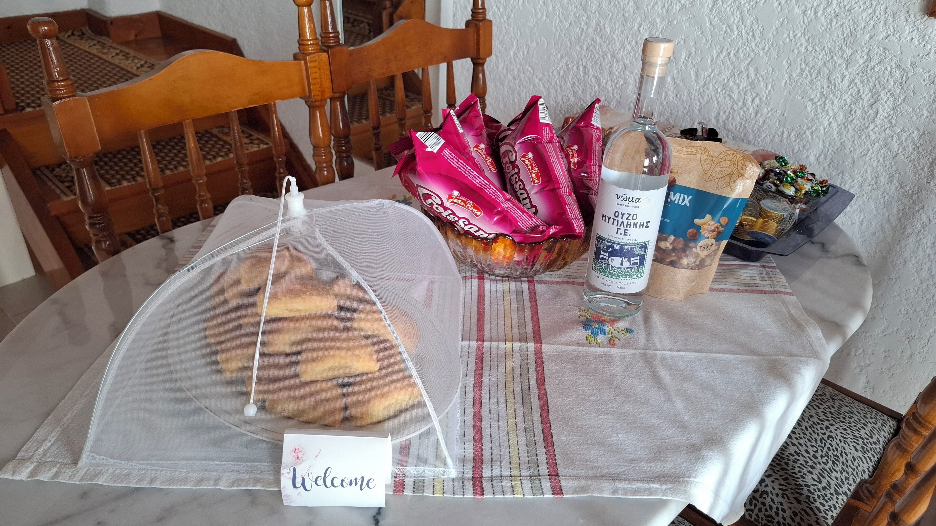 Taula amb una cistella plena de pa, una ampolla de licor i alguns estris envasellats.