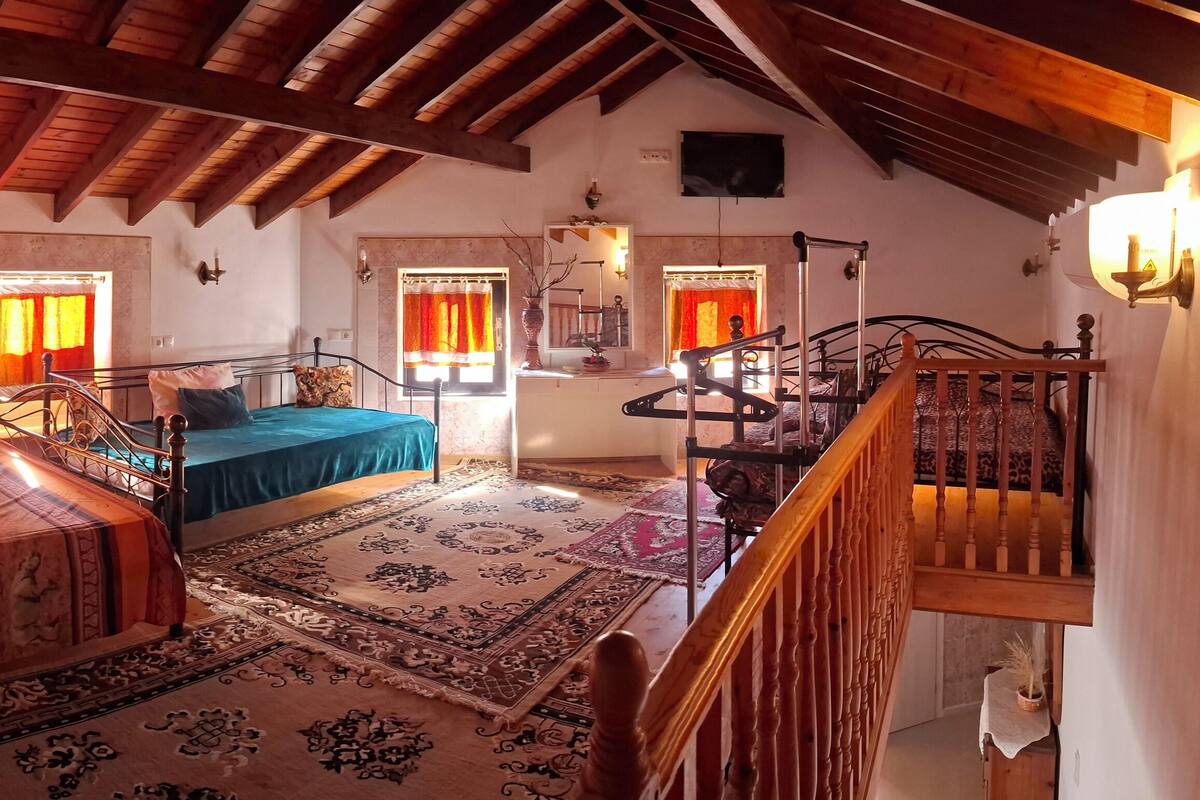 A bedroom with a large bed, a smaller bed, a staircase, and a view of the outside.