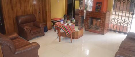 A living room with a brown leather sofa, a wooden coffee table with a striped tablecloth, and a brick fireplace.
