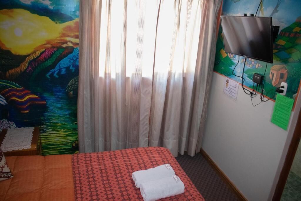 Une chambre d’hôtel avec un lit, des rideaux, un téléviseur fixé au mur et une fresque colorée sur le mur.