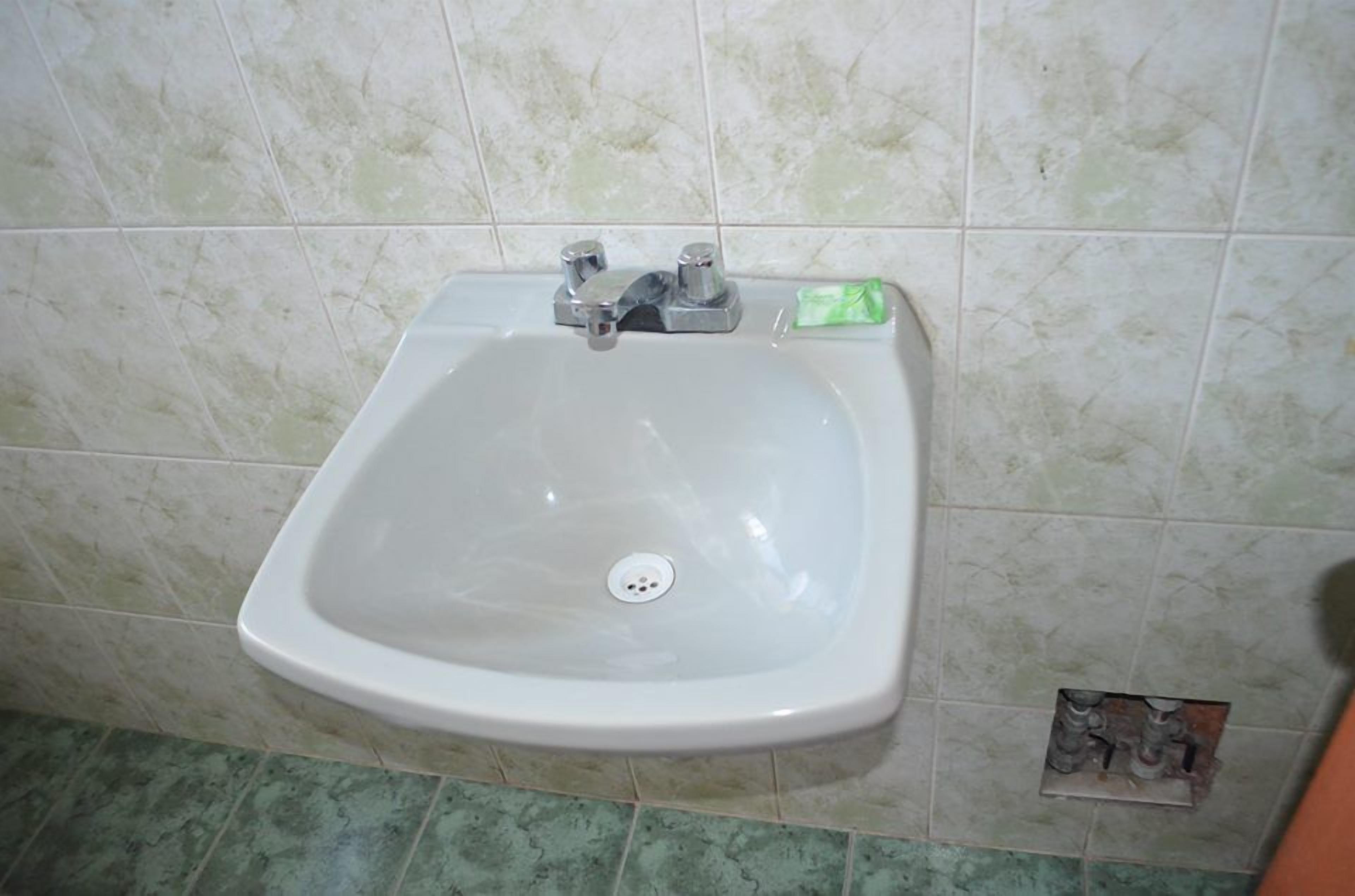 A bathroom with a white sink, a green soap dispenser, and a tiled floor.