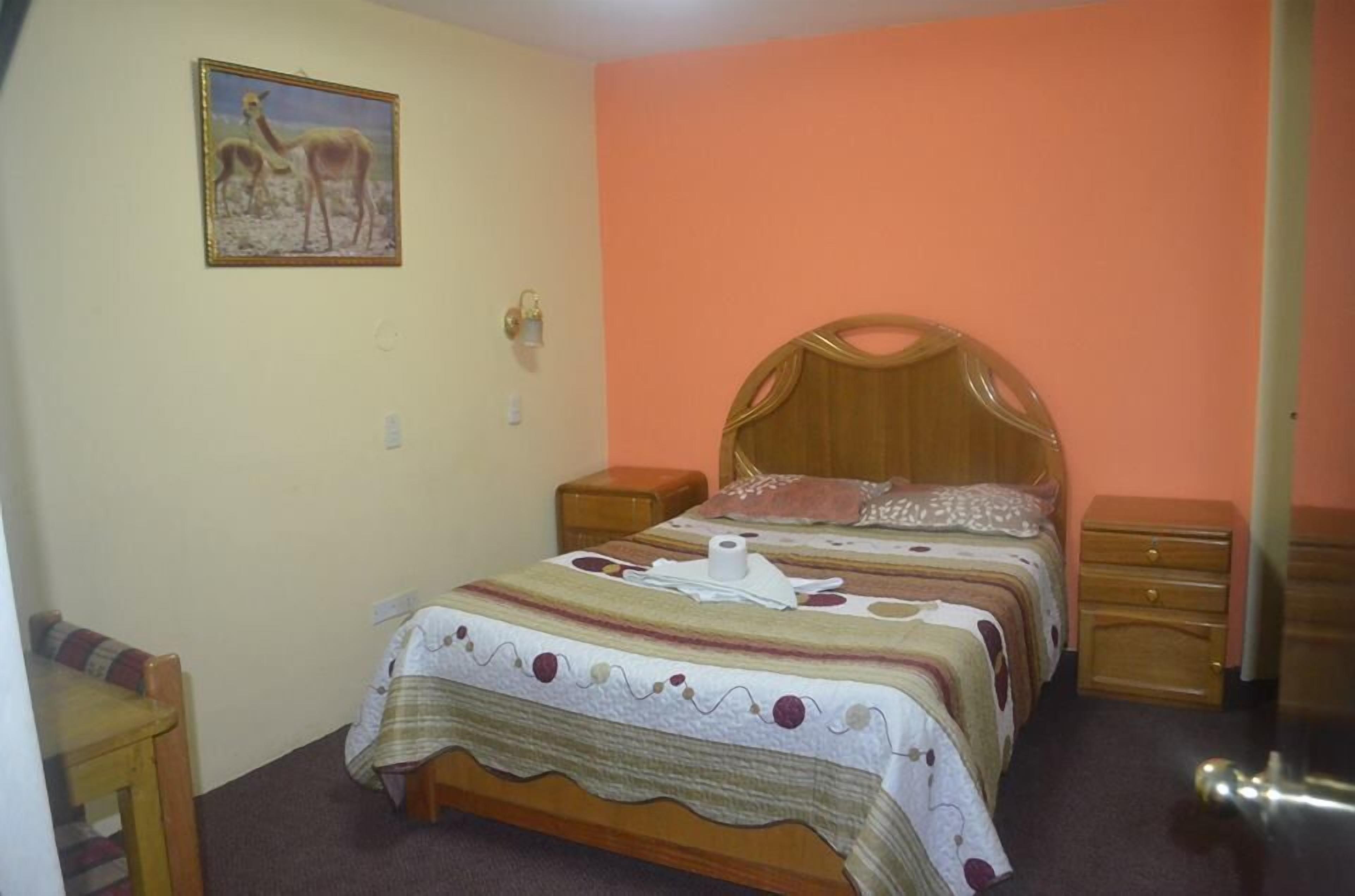A bedroom with a wooden bed, two nightstands, a wall-mounted lamp, and a painting of animals.