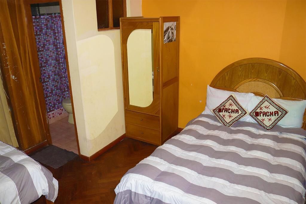 A room with two beds, a wooden wardrobe, and a bathroom visible through an open door.