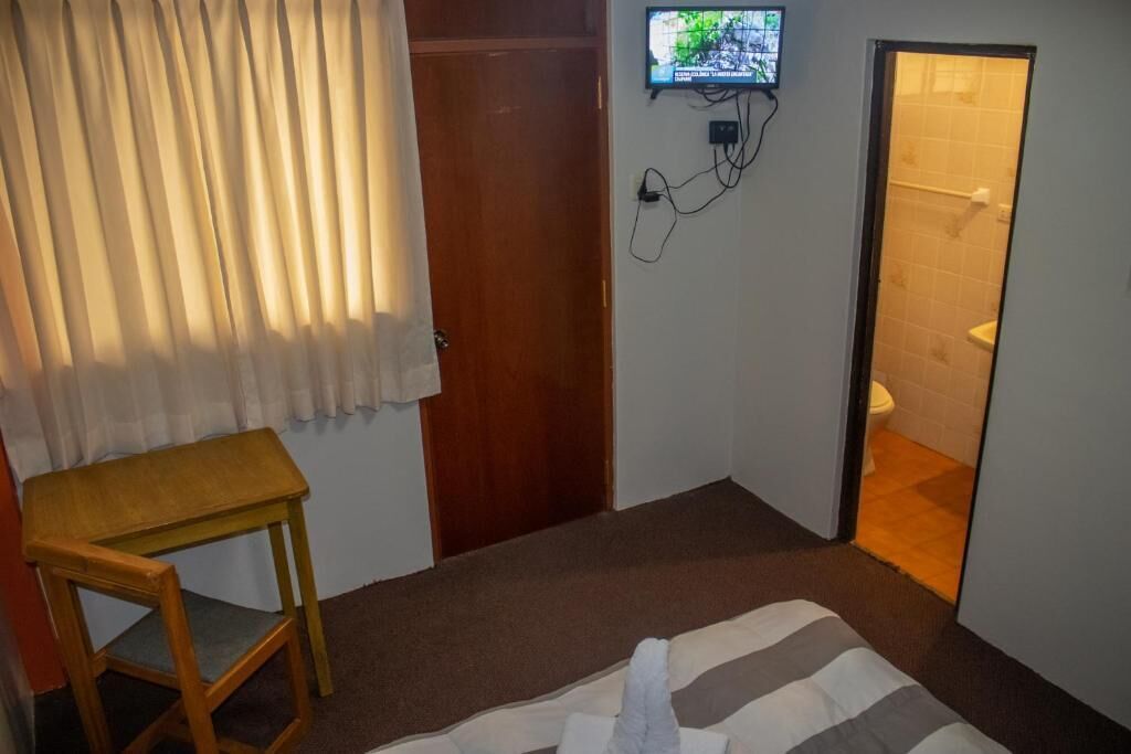 Et lille værelse med en træstol, et fjernsyn ophængt på væggen og en dør til et badeværelse.