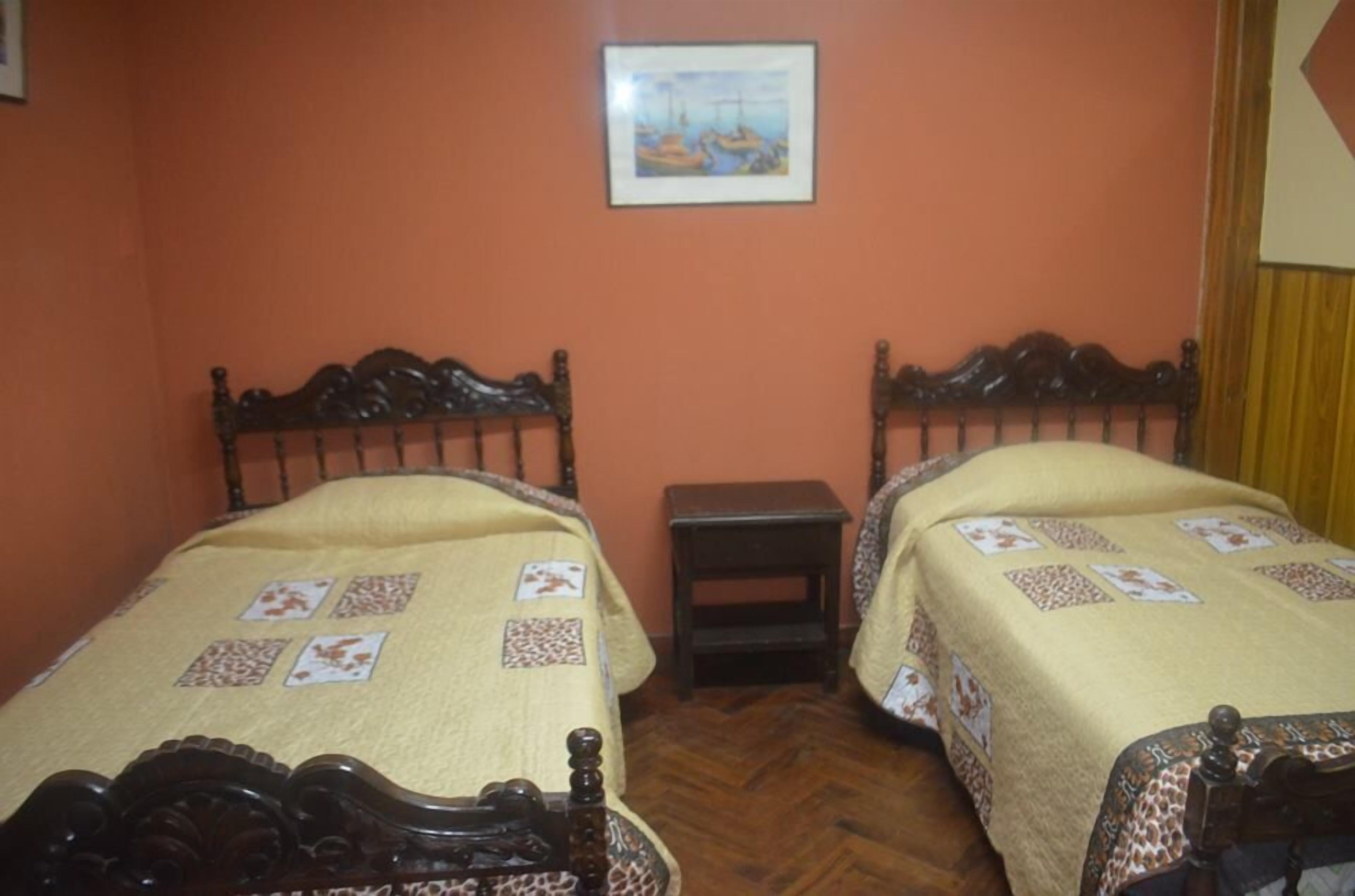 Quarto com duas camas de madeira, cada uma com colcha estampada, uma pequena mesa de cabeceira e um quadro na parede.