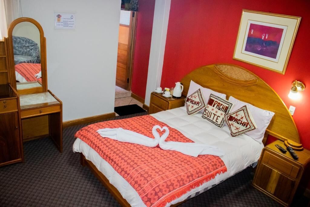 A hotel room with a bed, a wooden dresser, a mirror, a nightstand, and a framed picture on the wall.