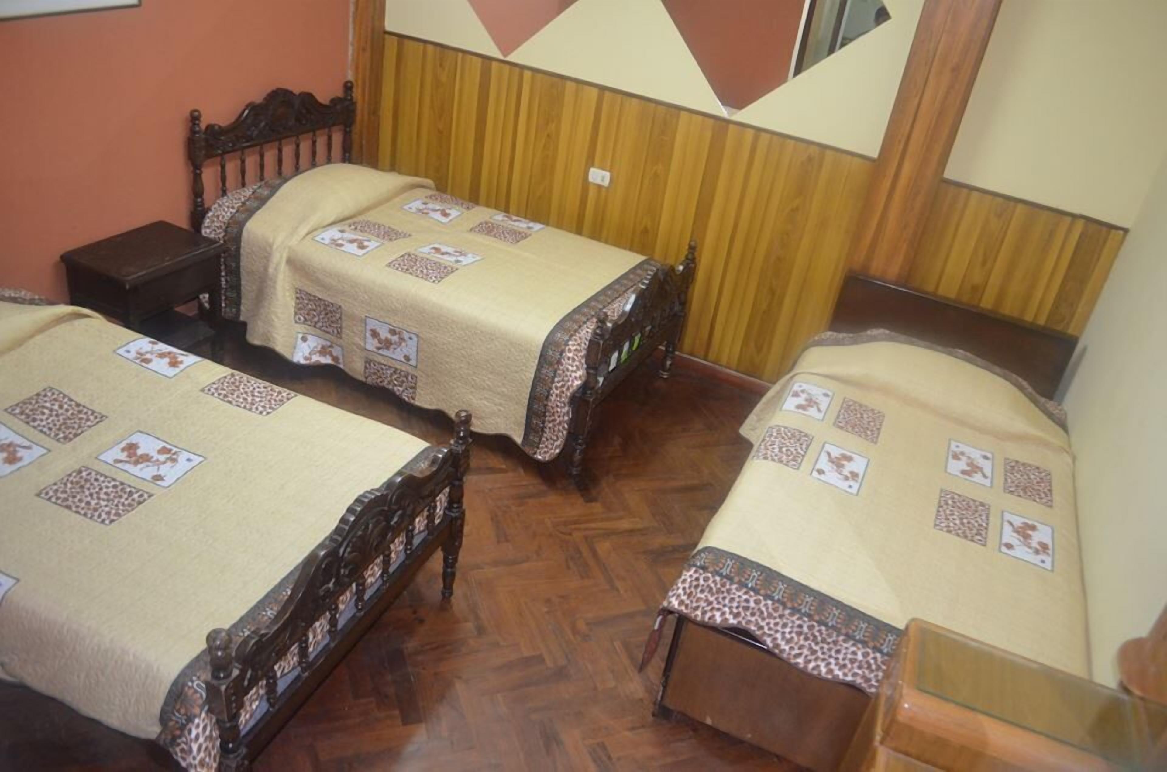 A room with two wooden beds, each with a patterned bedspread and a nightstand.