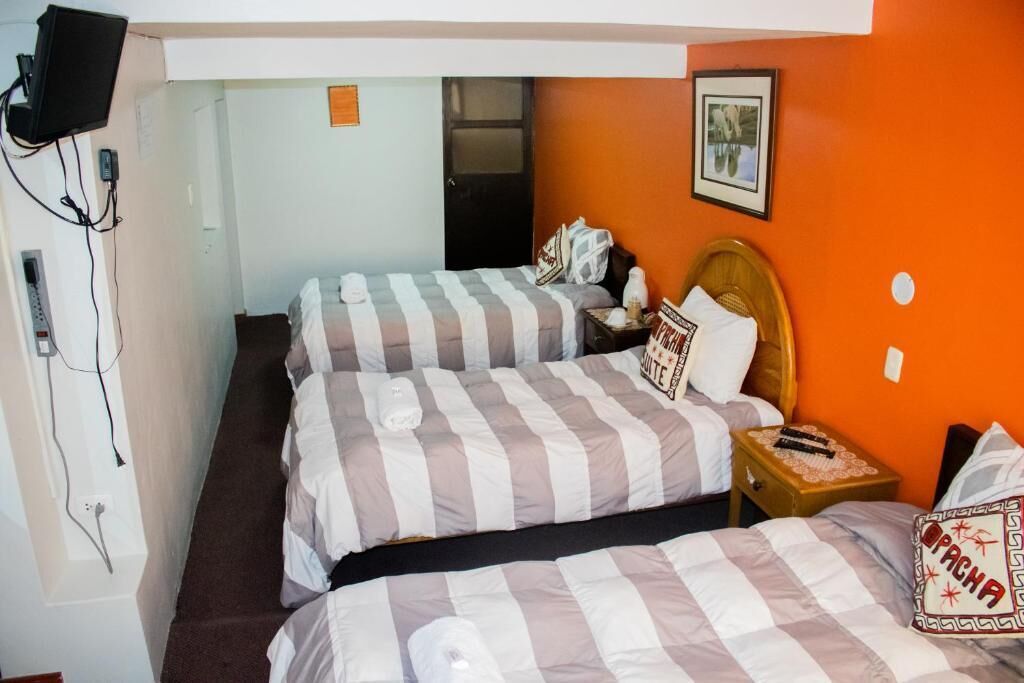 A hotel room with two beds, a television mounted on the wall, and a small table with a lamp.