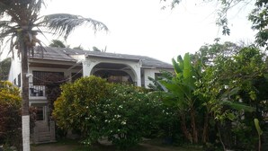 A house with a covered porch, surrounded by lush greenery and a palm tree. - Ground Road Native Place (San Andrés)