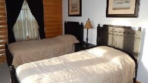 Un dormitorio con dos camas individuales, una mesita de noche con lámpara, un aparador y un cuadro en la pared.