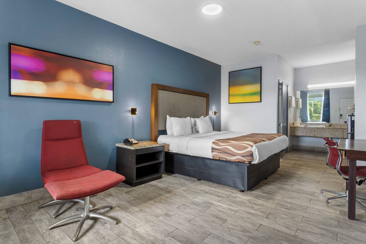 A hotel room with a bed, a desk, a chair, and artwork on the walls.