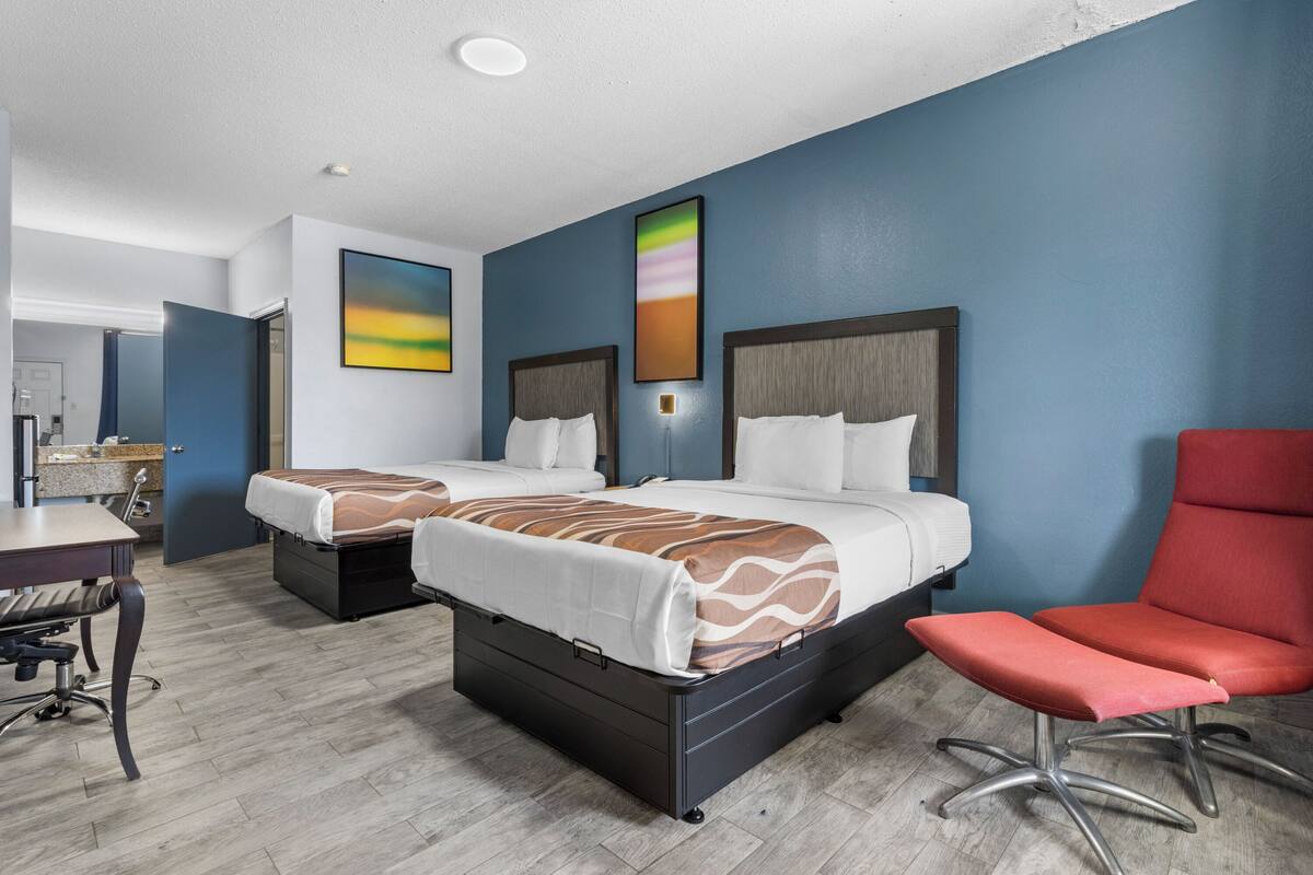 A hotel room with two beds, a desk, and a red chair.