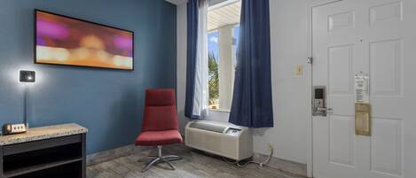 Une pièce avec un mur bleu, une chaise rouge, un radiateur, une porte et une fenêtre avec des rideaux.