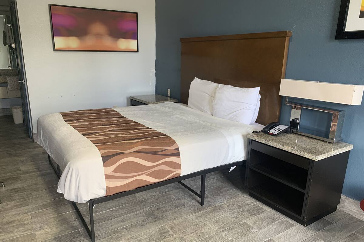 A hotel room with a bed, a nightstand, a telephone, and a painting on the wall.