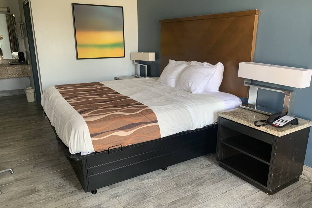 A hotel room with a bed, bedside tables, a lamp, a phone, and a painting on the wall.