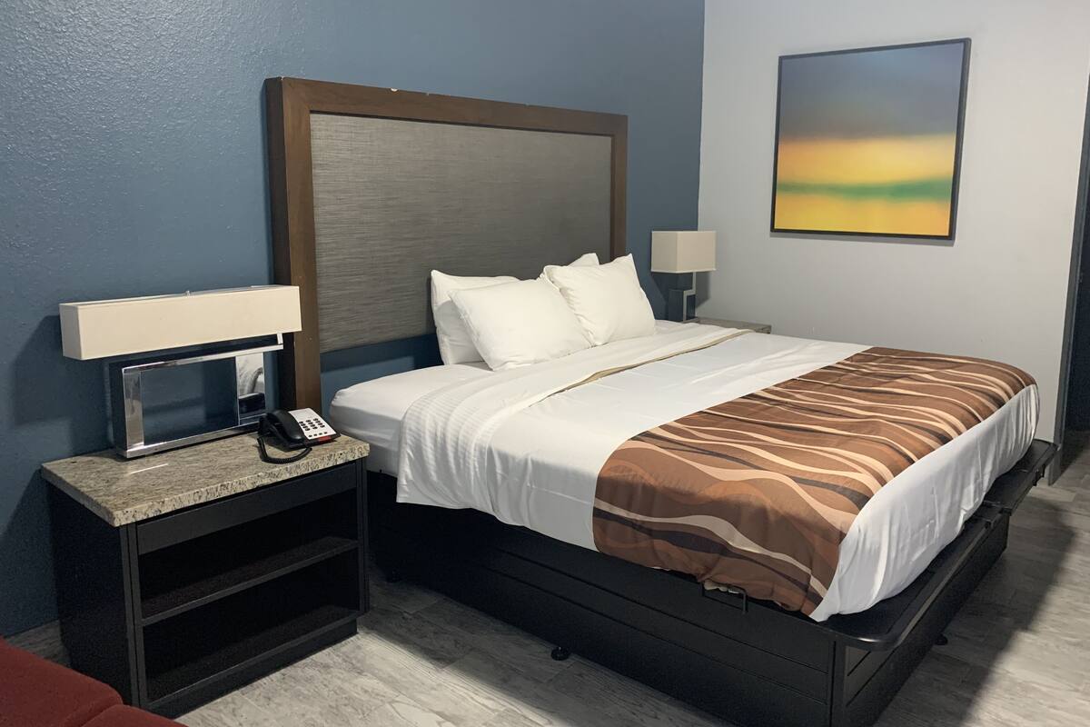 A hotel room with a bed, bedside tables, a lamp, a phone, and a painting on the wall.