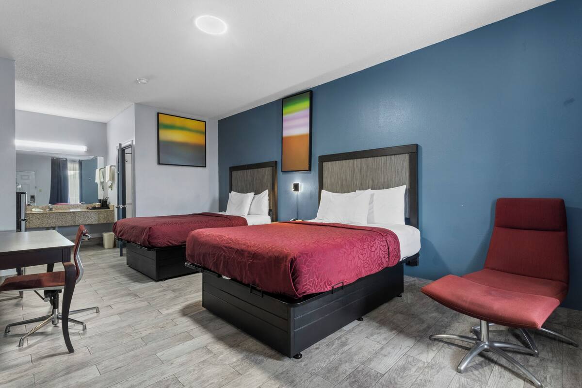A hotel room with two beds, a desk, a chair, and artwork on the walls.
