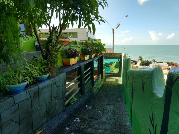 A narrow pathway leading to a beach with a view of the ocean. There are potted plants along the pathway and a mural depicting a beach scene.