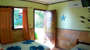 Ein Zimmer mit einem Bett, einem kleinen Tisch, einem fensterbelaubten Fenster und einer Wand-Klimaanlage.