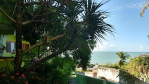 Ein Weg führt zu einem Strand mit Blick auf das Meer, umgeben von üppiger Vegetation und einem grünen Zaun.