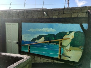A mural of a coastal scene with a wooden railing, a boat, and a small house. - Bamboo Flat Residencial (Natal)