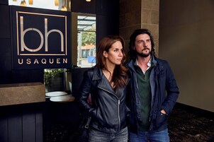A couple standing in front of a building with a sign that reads "bh USAQUEN".