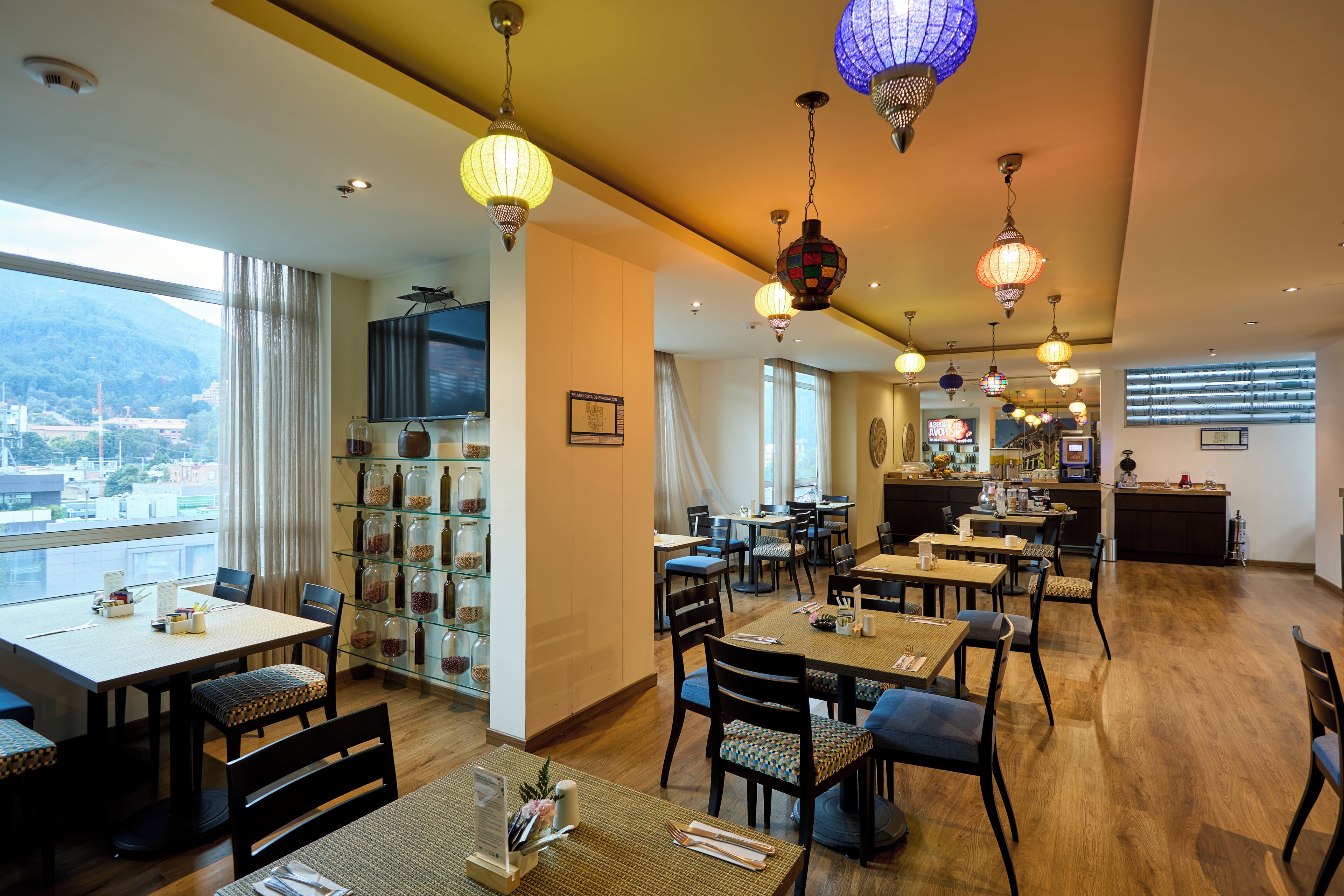 Un comedor de hotel con varias mesas y sillas, un bar y vistas a la ciudad.