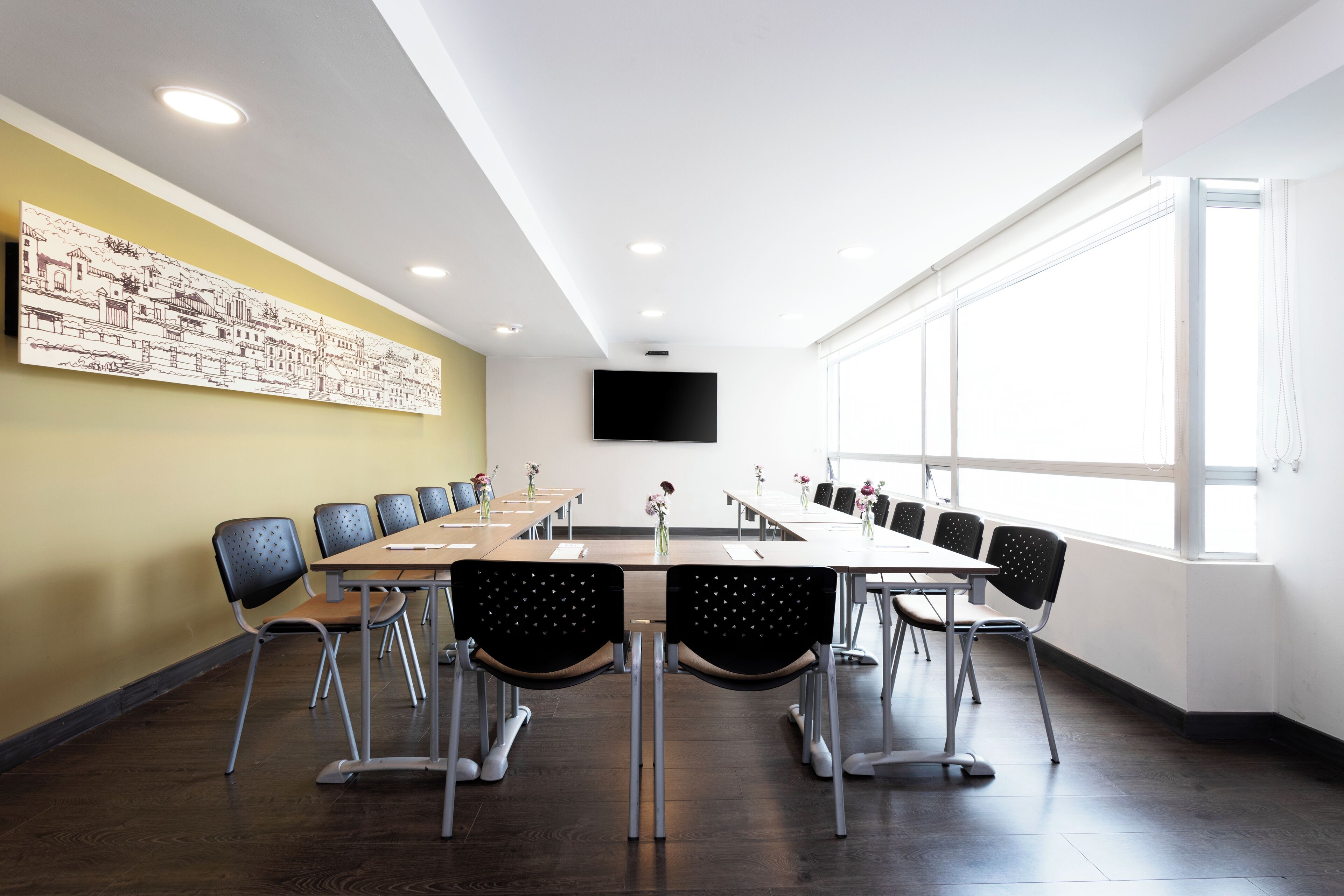 A conference room with a long table, chairs, a flat-screen TV, and a large window.