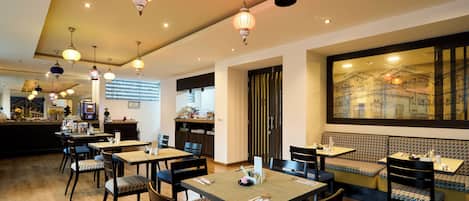 A restaurant with multiple dining tables and chairs, a kitchen area, and a large window with a cityscape view.