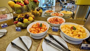 Een buffet met diverse soorten fruit en groenten, waaronder ananas, meloen en wortels, met aanduidingen zoals 'FRUTAS' en 'MELON'.