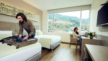 Quarto de hotel com cama, escrivaninha e uma grande janela com vista para a cidade.