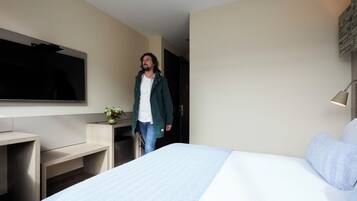 Une chambre d’hôtel moderne avec un grand lit, un téléviseur à écran plat fixé au mur, un bureau et une petite plante.
