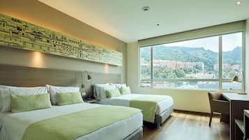 Ein Hotelzimmer mit zwei Betten, einem Schreibtisch und einem großen Fenster mit Blick auf die Stadt.