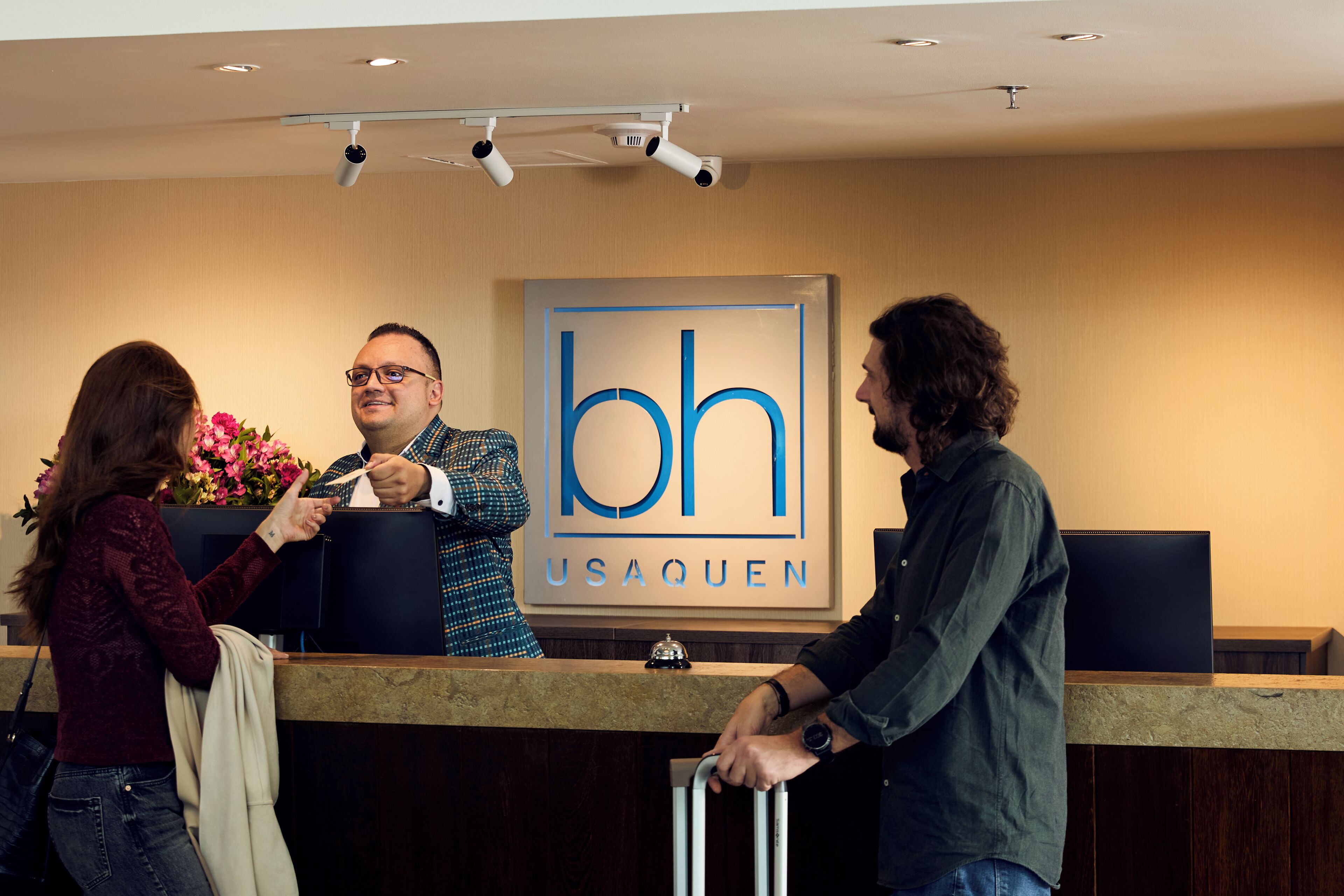 A reception desk with a sign reading "bh USAQUEN" and a camera mounted on the ceiling.