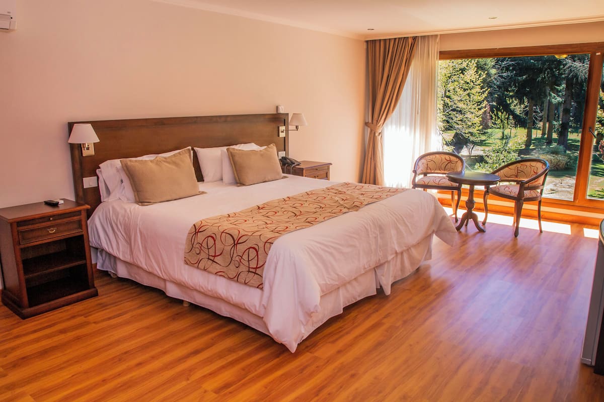 A hotel room with a large bed, bedside tables, a desk with chairs, and a view of the outdoors.