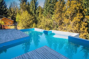 Surrounded by a lush forest, this pool area offers a natural and tranquil setting with a wooden deck and a charming cabin in the background.