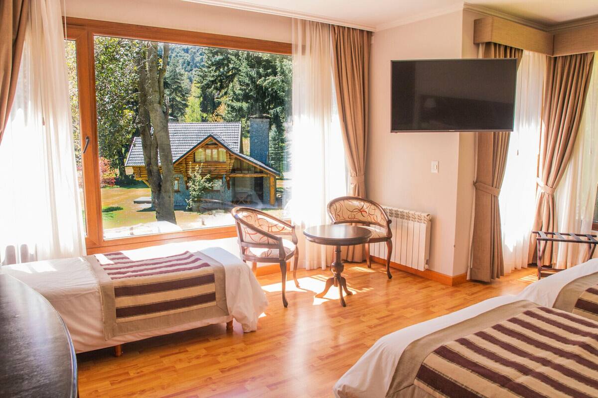 A hotel room with two beds, a TV, a table, and a chair.