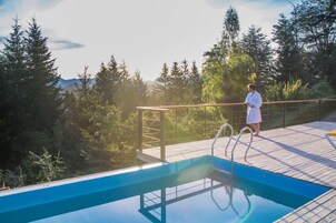 A wooden deck with a pool, surrounded by trees and mountains in the background.