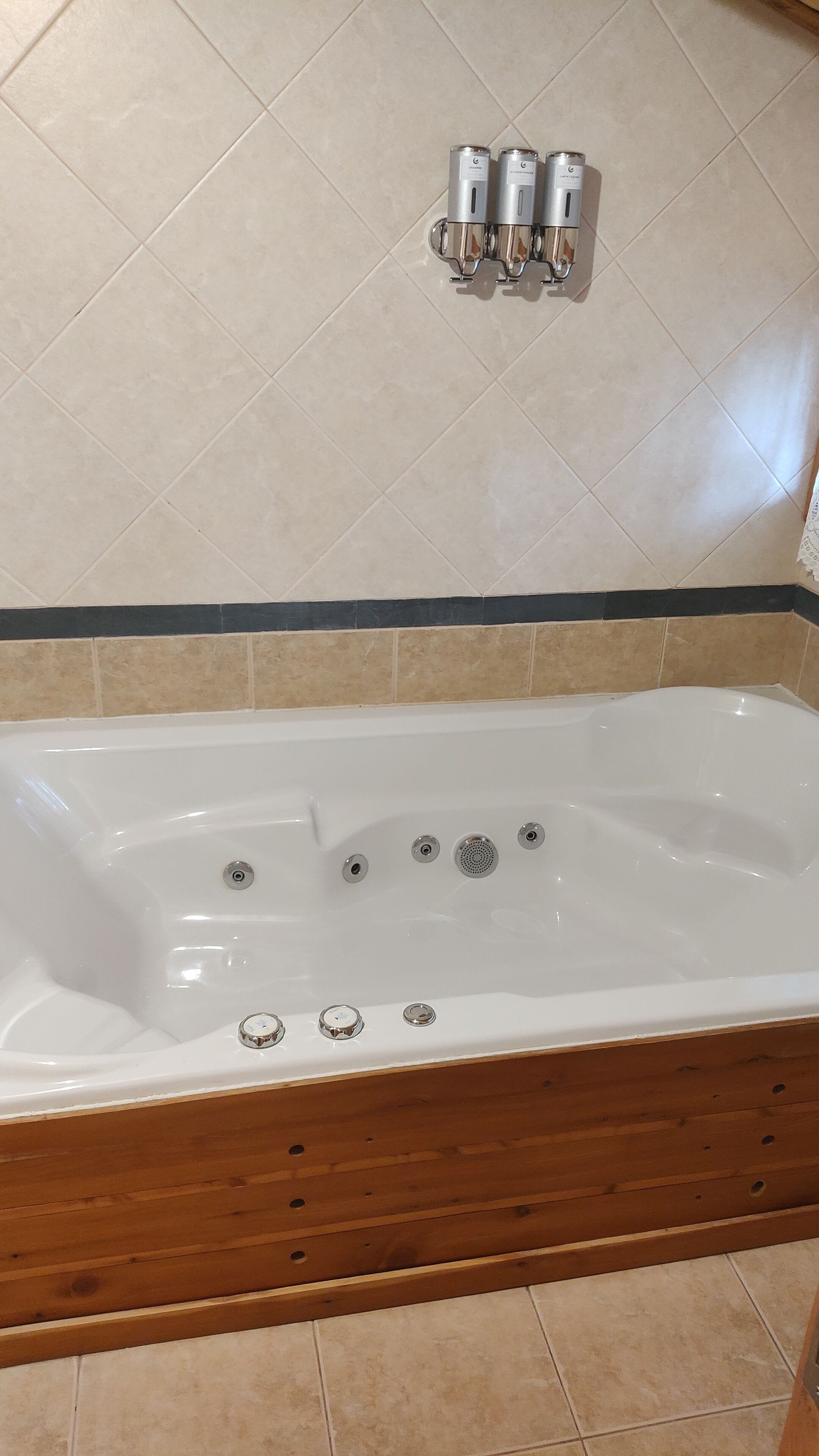 A bathroom with a white bathtub, three faucets, and a wooden floor.