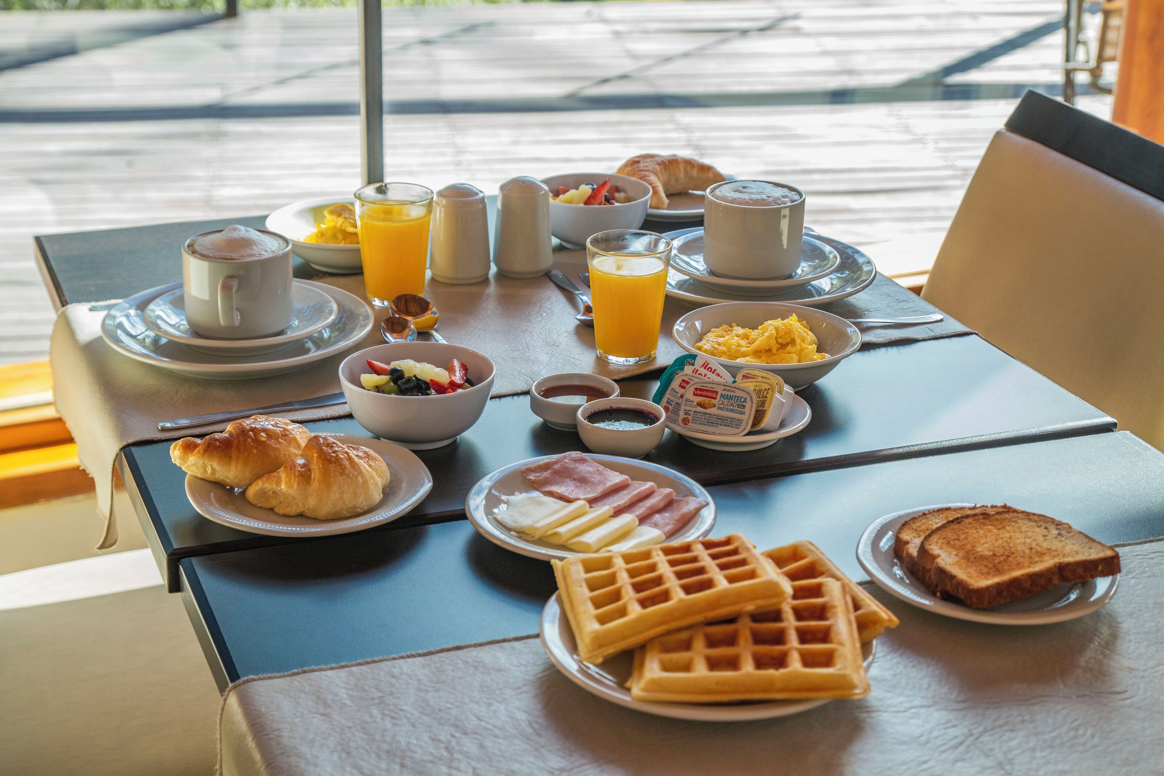 A breakfast table with croissants, waffles, eggs, and orange juice.