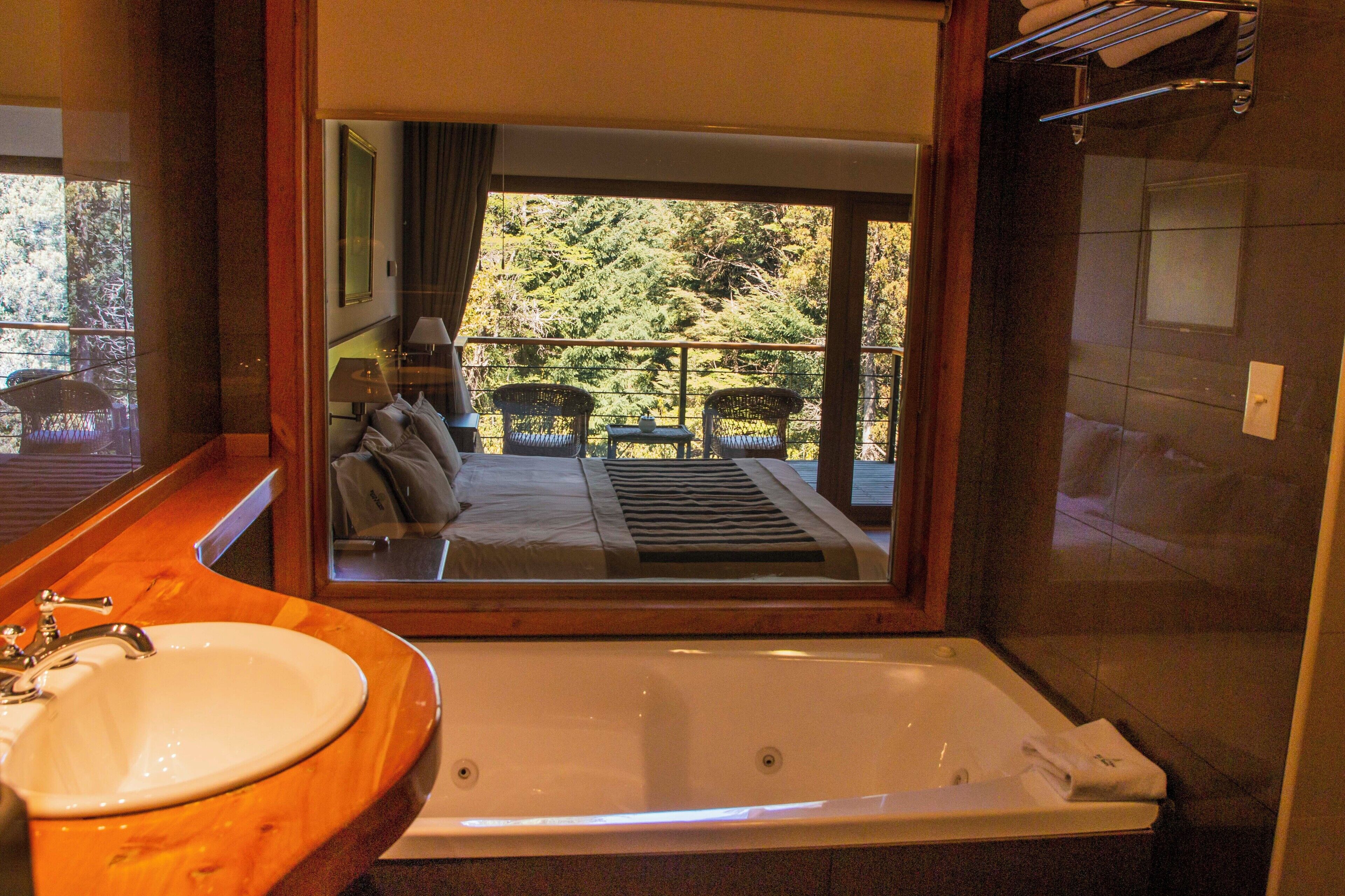 A bathroom with a large bathtub, a wooden vanity, and a view of a balcony with outdoor furniture.