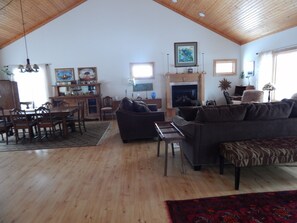 A spacious living room with a high ceiling, wooden floors, a fireplace, a dining area with a wooden table and chairs, and a large sofa.