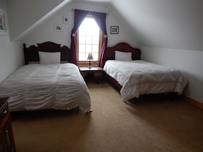 A bedroom with two single beds, a small table, and a window with curtains.