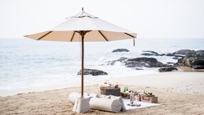 Une plage avec un grand parasol, un coin pique-nique et une vue sur l’océan.