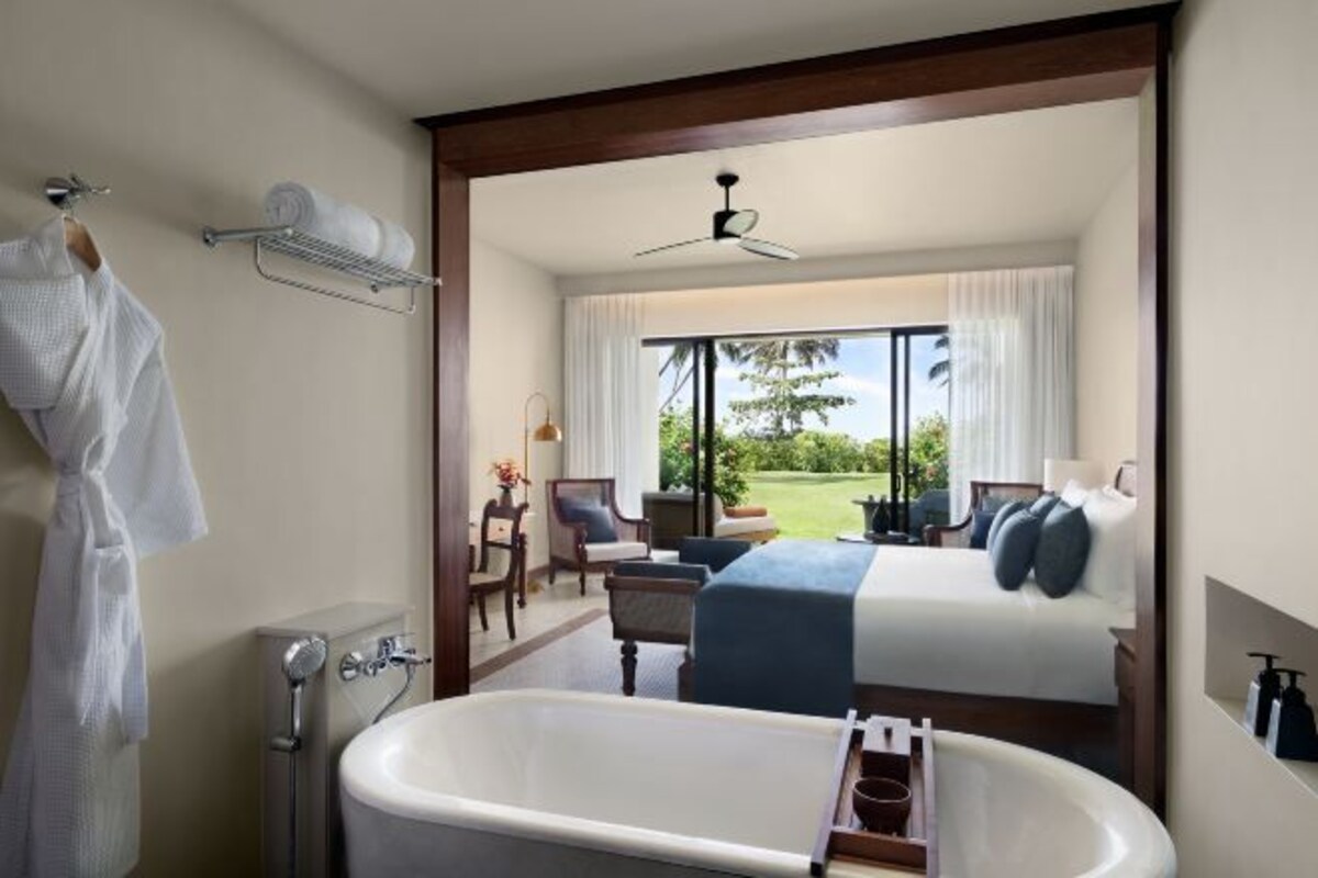 Une chambre d’hôtel dotée d’une grande baignoire, d’un lit recouvert d’une courtepointe bleue, offrant une vue sur un terrain de golf et comprenant un balcon avec une chaise et une table.