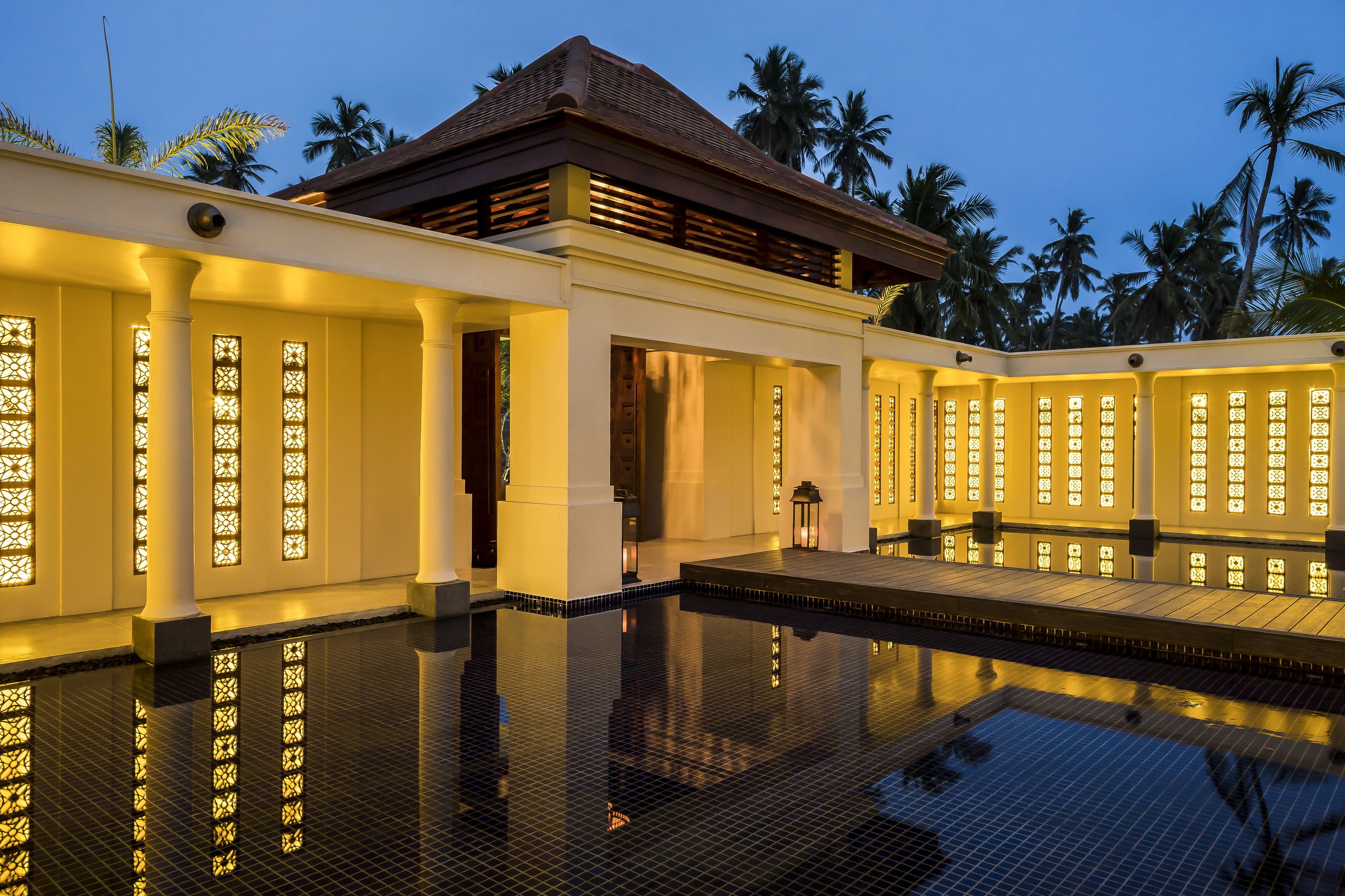 A modern hotel with a pool, columns, and palm trees in the background.