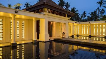 A modern hotel with a pool, columns, and palm trees in the background.